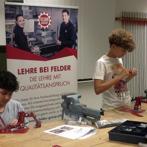 zwei Schüler beim Montieren eines hydraulischen Baggers