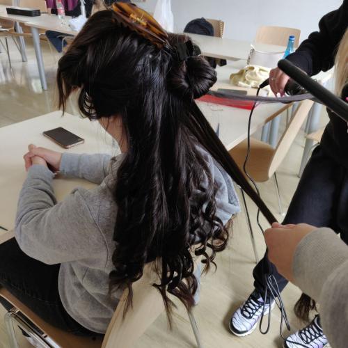 Eine Schülerin bearbeitet die langen Haare einer Mitschülerin mit dem Lockenstab