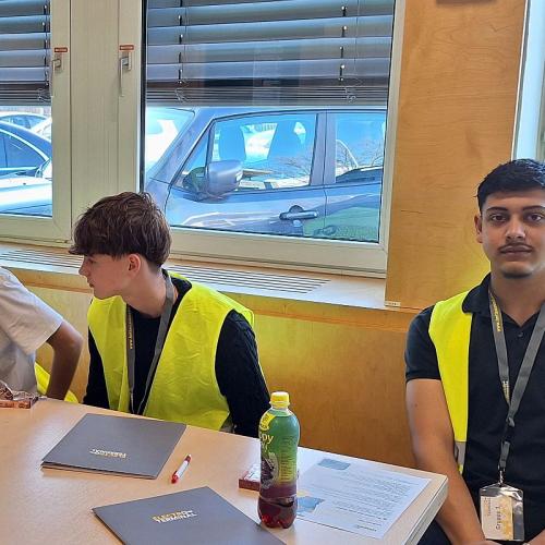 Bild zeigt drei Schüler an einem Tisch sitzend mit gelben Warnwesten