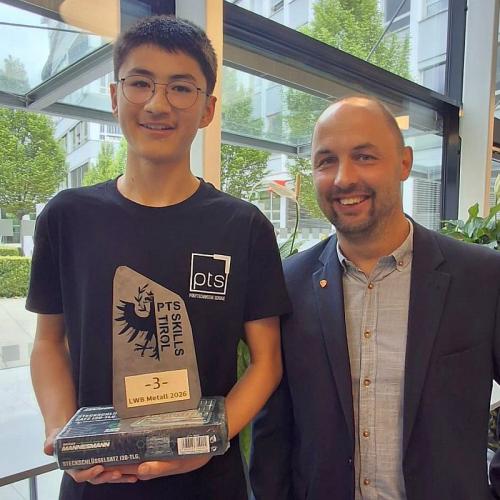 Bild zeigt einen Schüler und einen Lehrer im Festsaal bei einer Siegerehrung