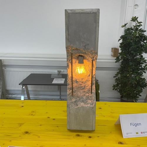 Bild zeigt einen länglichen Block aus Beton der in der Mitte bruckartig eingetieft ist an dieser Stelle befindet sich eine Glühlampe