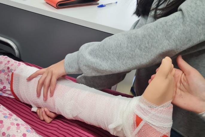 Bild zeigt wie eine Schülerin einer speziellen Puppe für die Pfegeausbildung einen Verband anlegt