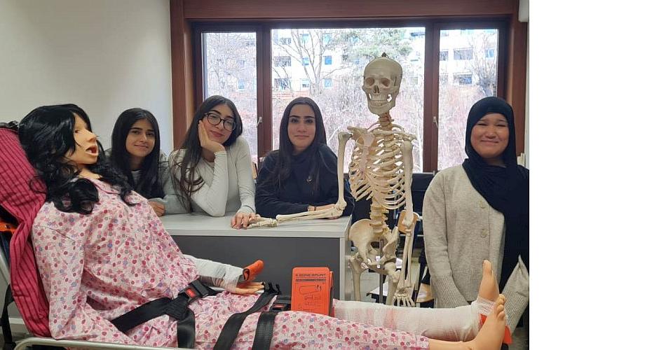 Bild zeigt vier Schülerinnen der Pflegegruppe im Vordergrund ist die neue Pflegepuppe Sam und das Skelett Jack
