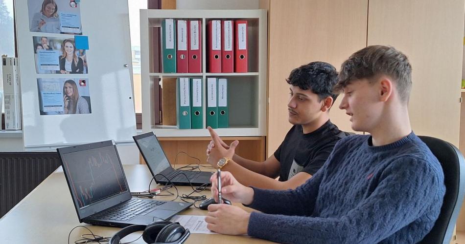 Bild zeigt 2 männliche Schüler bei typischen Arbeiten in einem Büro mit Laptops und Aktenordnern