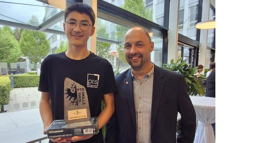 Bild zeigt einen Schüler und einen Lehrer. Der Schüler hält den Preis für den 3. Platz in Metalltechnik in der Hanb