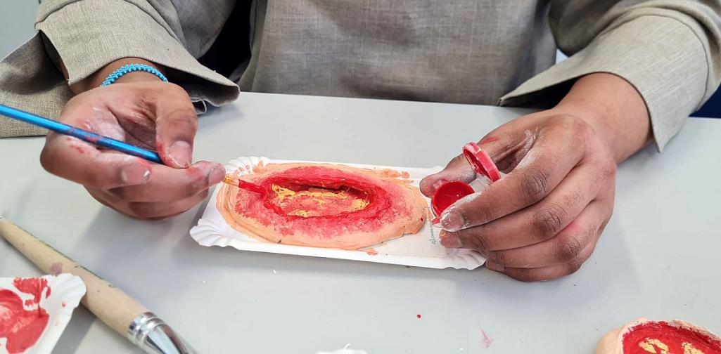 Bild zeigt einen Schülerin beim Gestalten einer Wunde aus weißem Ton und roter und gelber Farbe.